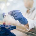 Close-up of a scientist wearing gloves and handling test tubes in a laboratory environment.