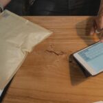 Person managing logistics on a tablet with a parcel on a wooden table.