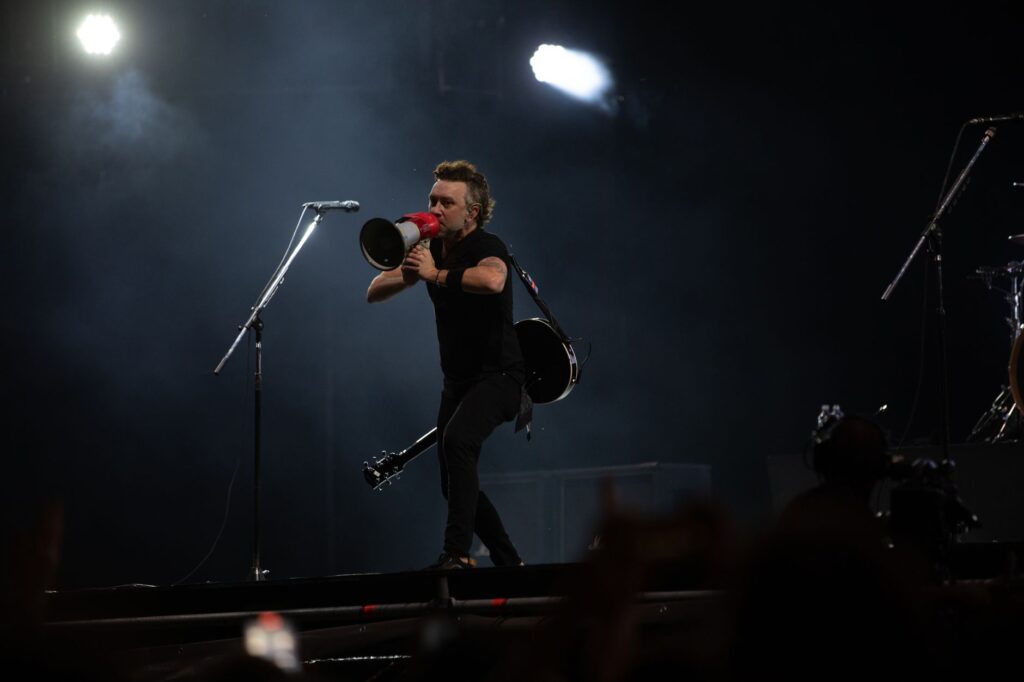 Musician with megaphone on stage during night concert, energizing the crowd.