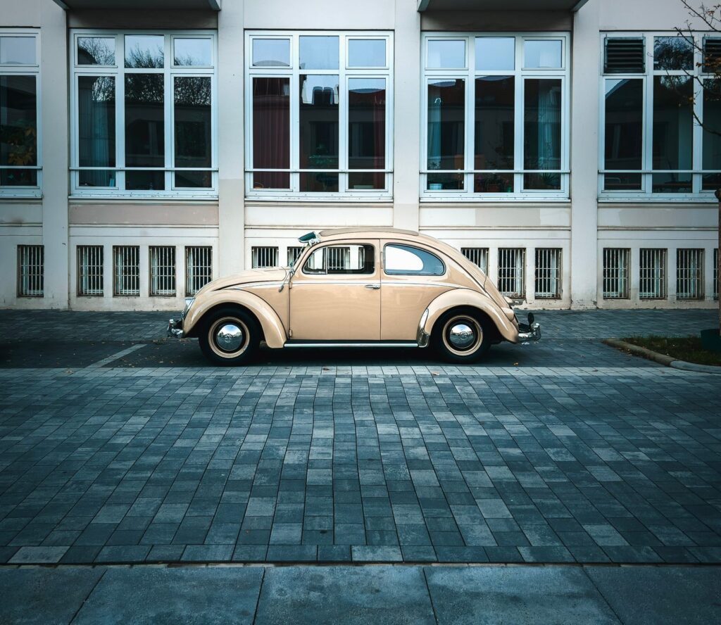 Side view of a classic beige Volkswagen Beetle parked in front of a building.