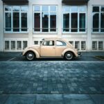 Side view of a classic beige Volkswagen Beetle parked in front of a building.