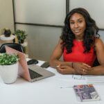 Professional woman sitting at a desk with laptop, papers, and plants in a modern office.