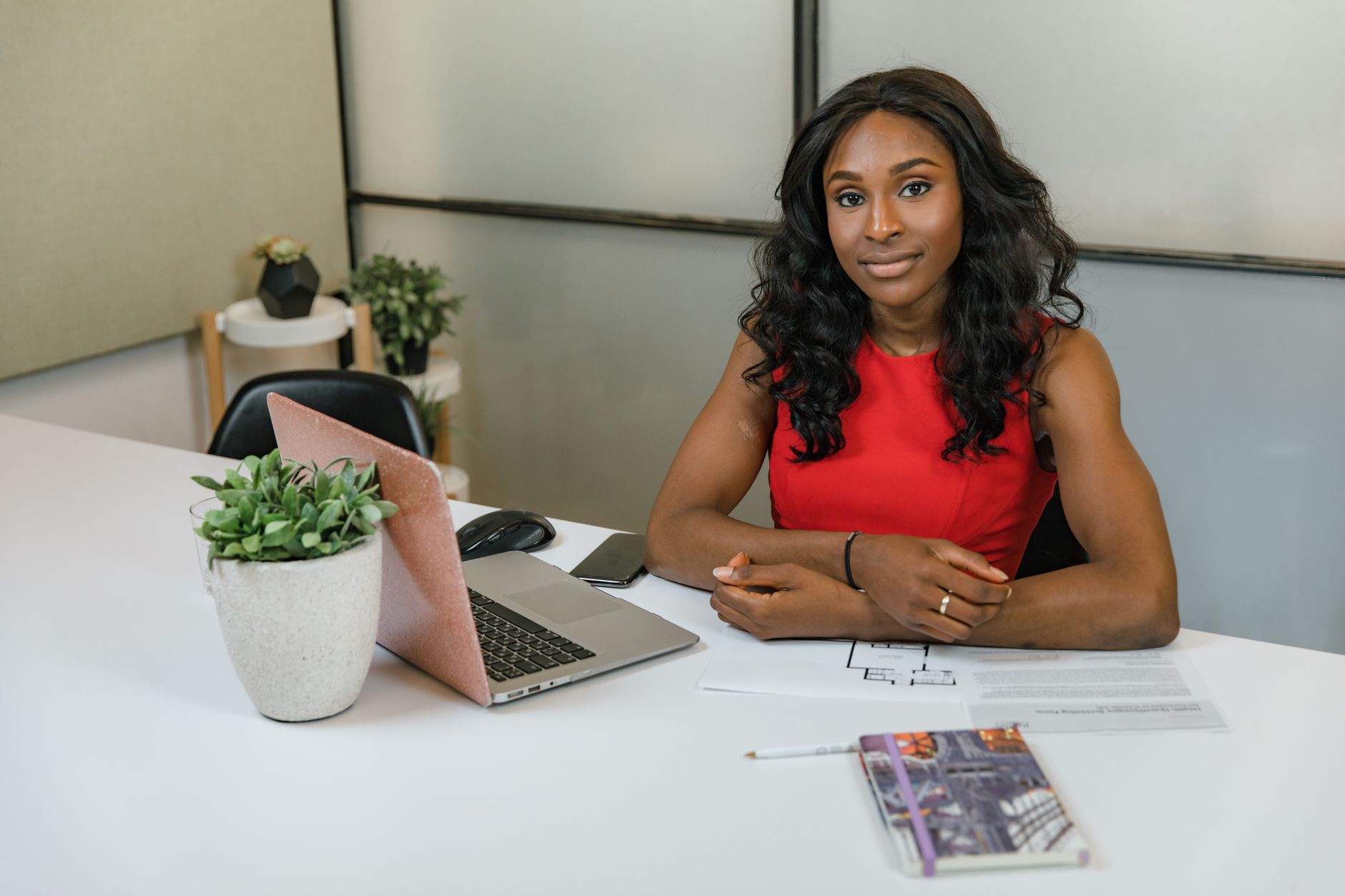 Professional woman sitting at a desk with laptop, papers, and plants in a modern office.