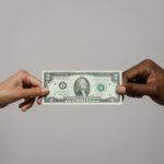 Two hands exchanging a two dollar bill, symbolizing financial transaction.