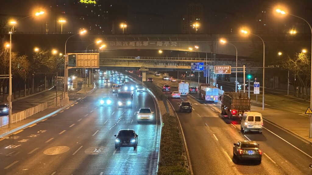 Traffic flows along a major Beijing highway, illuminated by bright streetlights at night.