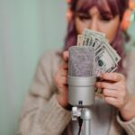 Adult woman with headset counting dollar bills in front of microphone indoors.