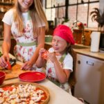 Happy mother and daughter making pizza together in a home kitchen, sharing quality family time.