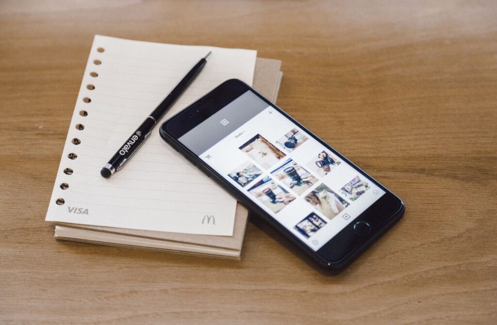 Modern flat lay featuring a smartphone, pen, and notebook on a wooden table.