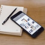 Modern flat lay featuring a smartphone, pen, and notebook on a wooden table.