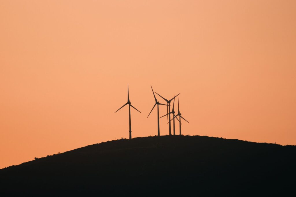 Wind turbines silhouetted against a vibrant yellow sunset sky on a rural hilltop.