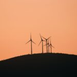 Wind turbines silhouetted against a vibrant yellow sunset sky on a rural hilltop.