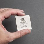 A close-up view of a person holding an Nvidia chip with a gray background.