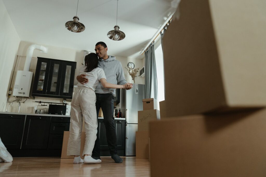 Happy couple dancing together in their new home filled with moving boxes, celebrating new beginnings.