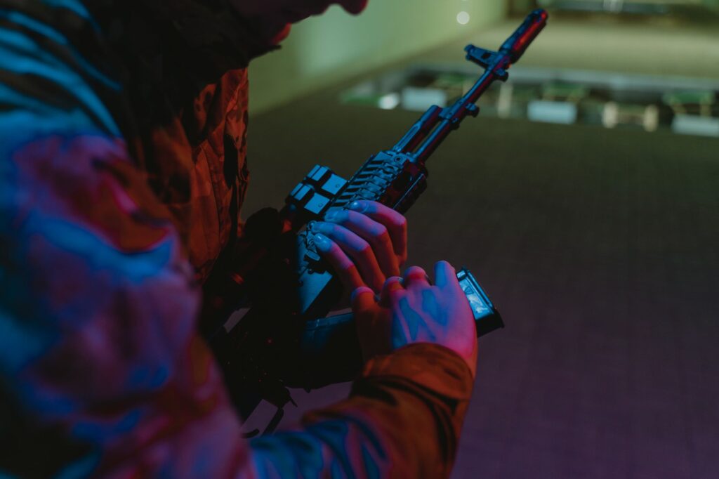 Close-up of a person handling a tactical rifle with colorful dramatic lighting.