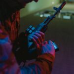 Close-up of a person handling a tactical rifle with colorful dramatic lighting.