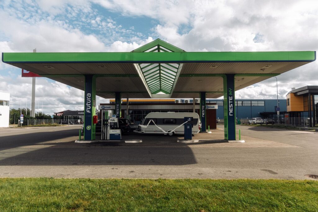 A modern gas station with a green canopy and parked camper van under a cloudy sky.