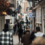 People walking through a narrow urban alley with shops and signs on both sides.
