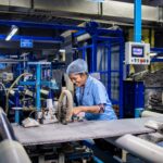 Indian female factory worker smiling while operating complex textile machinery in an industrial setting.
