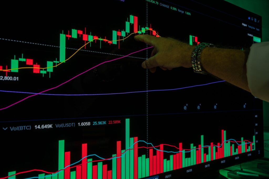 Close-up of a hand pointing to a stock market graph on a digital screen, highlighting trends.
