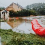 Flooded residential area protected by red flood barriers, showing severe weather impact.