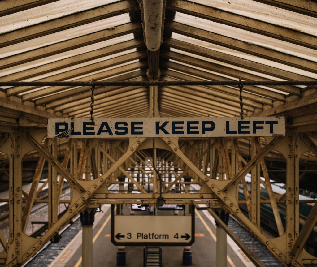 Vintage metal construction on railway station with platform under old roof and sign saying Please keep left