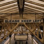Vintage metal construction on railway station with platform under old roof and sign saying Please keep left