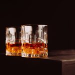 Two whiskey glasses with amber liquid on a dark surface, creating a cozy atmosphere.