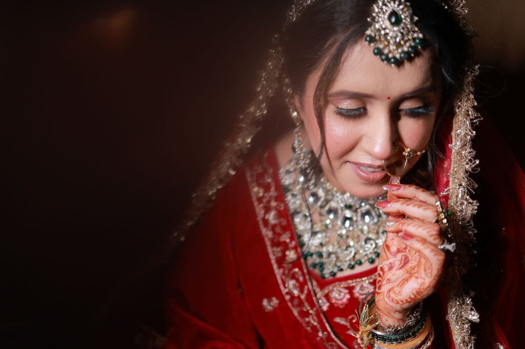 Portrait of a South Asian bride adorned in traditional red bridal attire, showcasing intricate jewelry and henna designs.