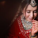 Portrait of a South Asian bride adorned in traditional red bridal attire, showcasing intricate jewelry and henna designs.