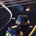 Detailed view of an electric guitar's volume knob with strings in the background.