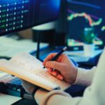Person analyzing financial data on screens, making notes. Ideal for business and finance themes.
