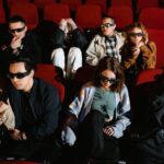 Group of people watching a movie in 3D glasses, expressing excitement and surprise.