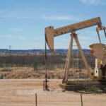 Industrial oil pumpjack in a desert setting under a clear blue sky, illustrating oil extraction technology.