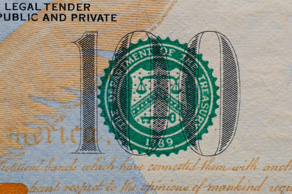 Detailed view of the US 100 dollar bill showing the Treasury seal and printed text.