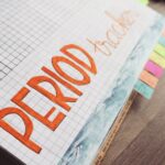 Close-up of a handwritten period tracker in a grid-lined journal on a wooden table.