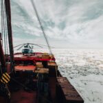 A helicopter on the deck of an icebreaker ship navigating through icy Arctic waters.