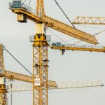 Cluster of yellow tower cranes at a construction site with a gloomy sky background.