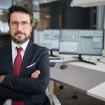 Business professional in corporate attire with arms crossed in a modern office space.