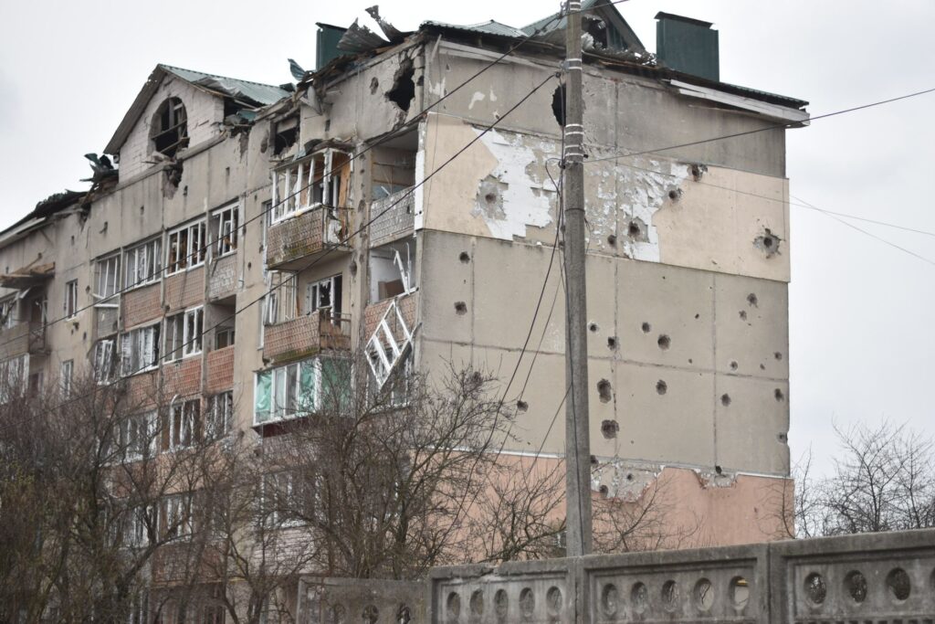 Damaged residential building with bullet holes and broken windows, highlighting war impact.