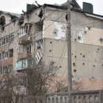 Damaged residential building with bullet holes and broken windows, highlighting war impact.