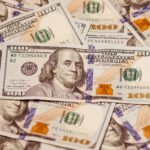 Close-up of multiple US hundred dollar bills featuring Benjamin Franklin, emphasizing wealth and finance.