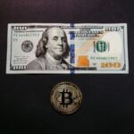 Image of a US 100 dollar bill and a Bitcoin coin on a black background, symbolizing traditional and digital currency.