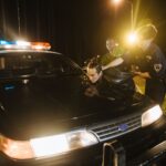 Police officers apprehending a suspect at night under streetlights by a patrol car.