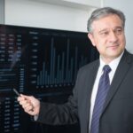 Professional man in suit reviewing financial charts on monitor, showcasing stock market trends.