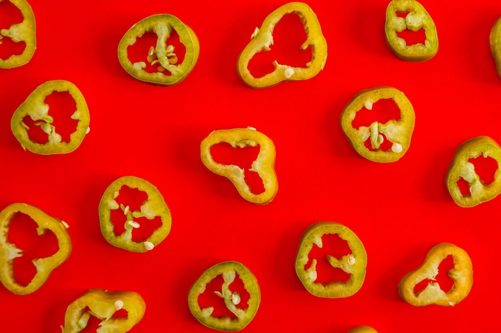 Fresh jalapeno slices laid out on a vivid red backdrop, perfect for spicy food concepts.