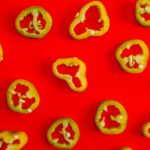 Fresh jalapeno slices laid out on a vivid red backdrop, perfect for spicy food concepts.