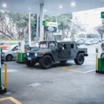 A rugged Hummer H1 parked at a busy gas station in an urban setting.
