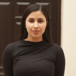 Portrait of a confident young woman standing in front of a dark brown door indoors.