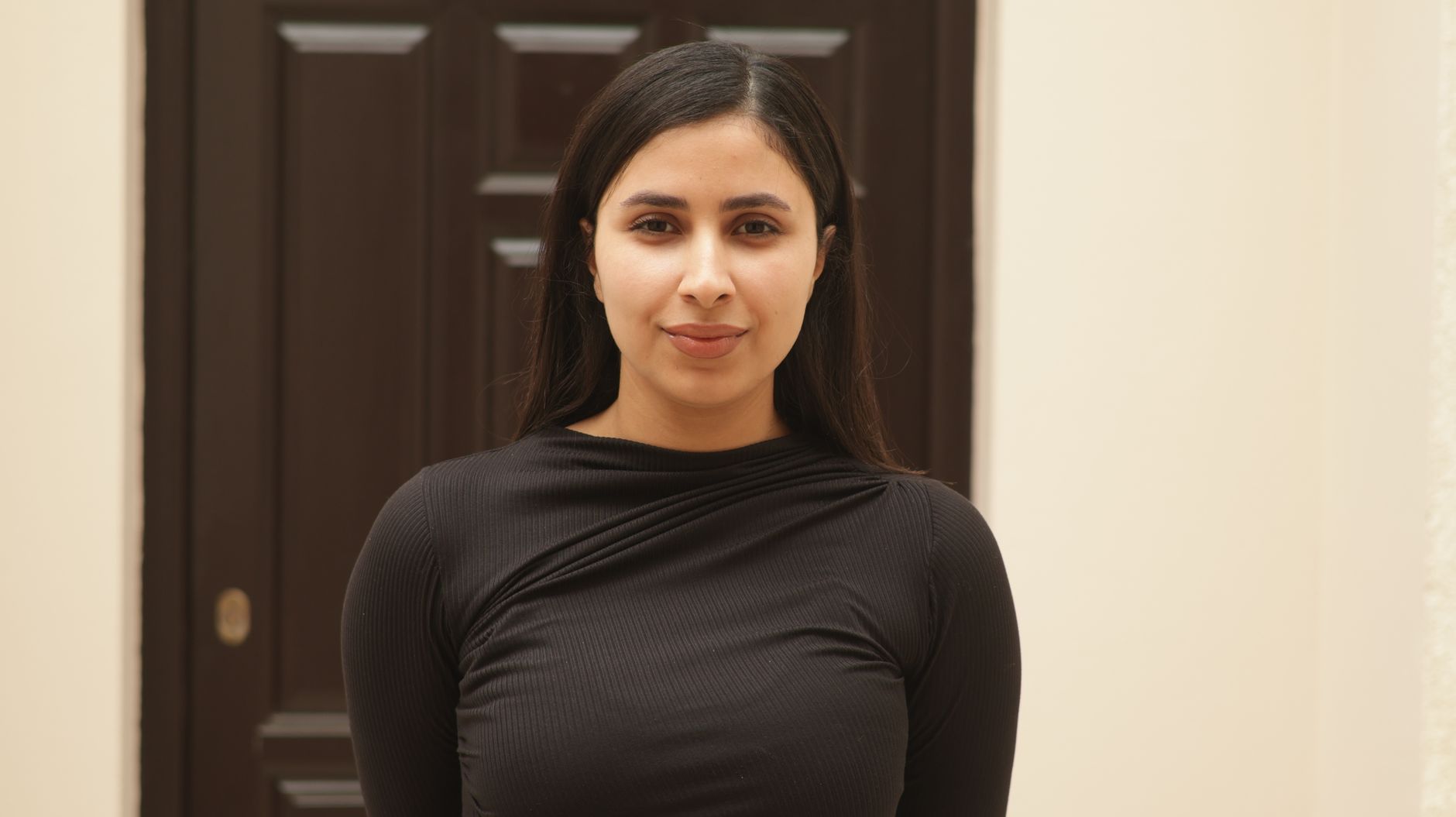 Portrait of a confident young woman standing in front of a dark brown door indoors.
