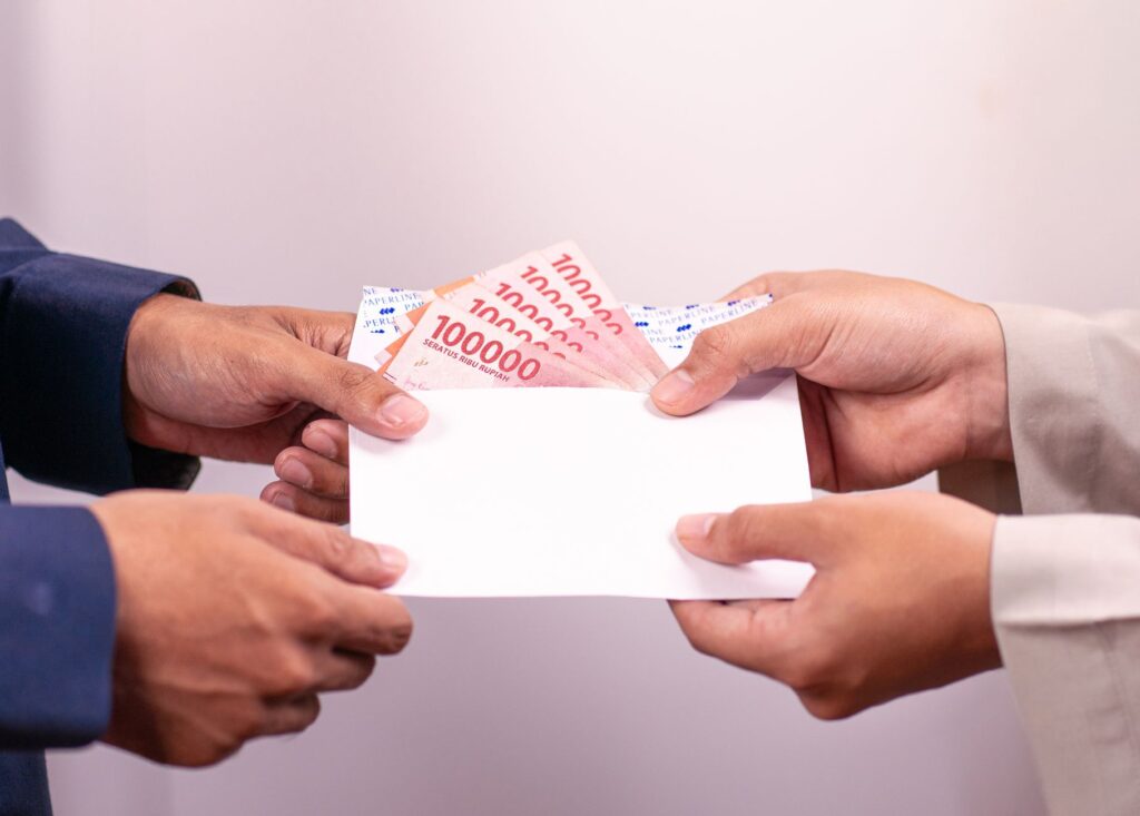 Hands exchanging an envelope with Indonesian Rupiah, highlighting financial transactions.